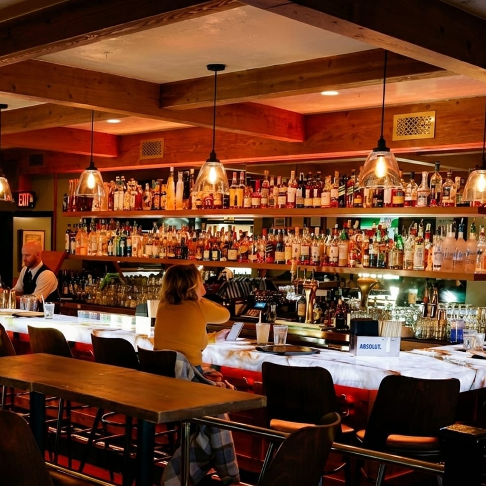 A cozy bar with a bartender, patrons, and shelves filled with various liquor bottles.