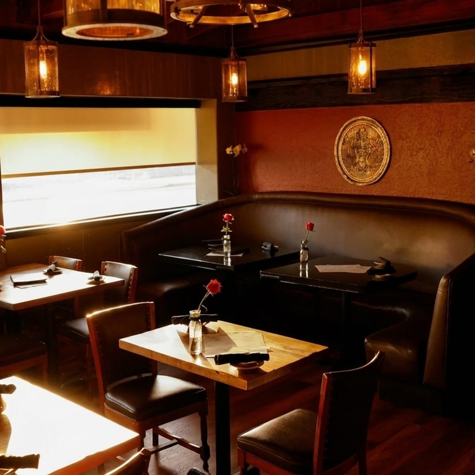 Warmly lit restaurant interior with wooden tables, leather chairs, and a long booth, featuring red roses.
